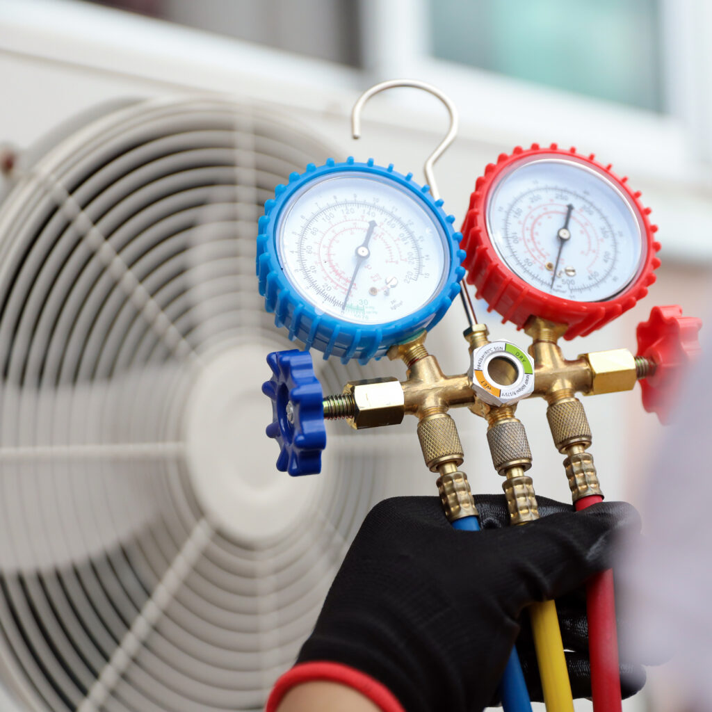 Air conditioning electrical technician using manifold gauge measuring tool checking refrigerant pump.